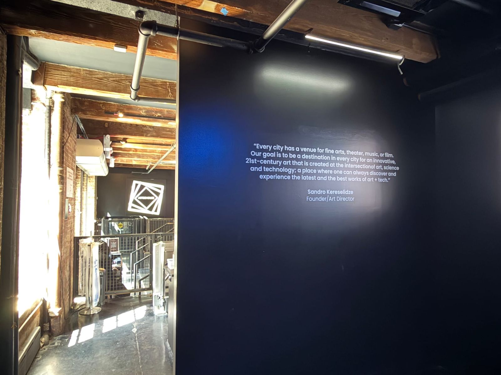 Entrance to ARTECHOUSE NYC with the founder's quote projected on a dark wall, daylight visible from the Chelsea Market side